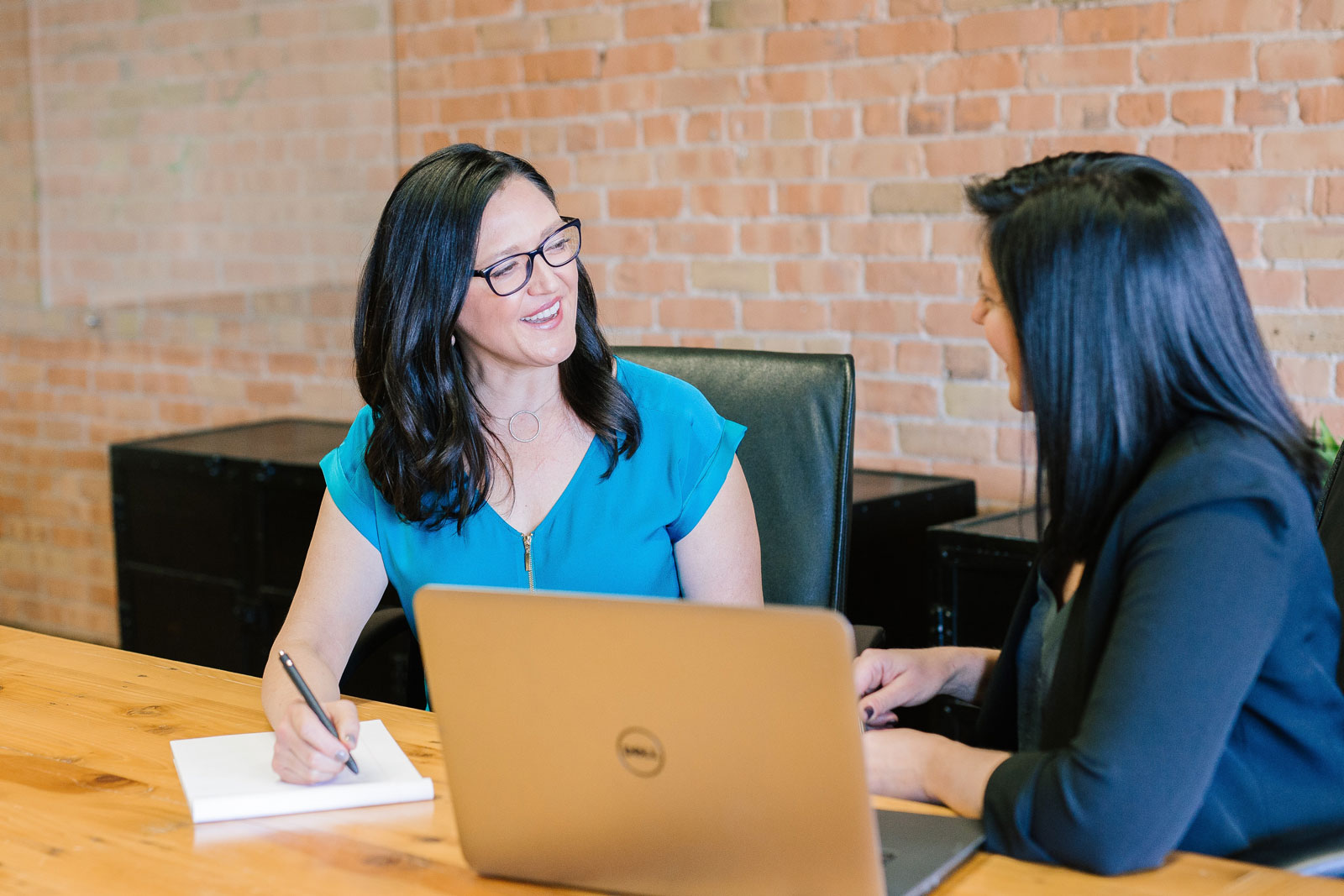 two professional women. One woman writing while other woman has laptop